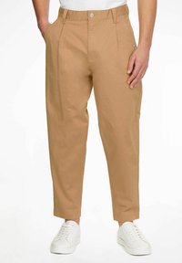 Pantalones de algodón color caqui con bolsillos laterales, corte recto y perneras ligeramente ajustadas. Cuenta con un cierre de botón y trabillas para el cinturón. Combinados con zapatillas blancas.