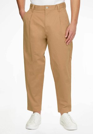 Pantalones de algodón color caqui con bolsillos laterales, corte recto y perneras ligeramente ajustadas. Cuenta con un cierre de botón y trabillas para el cinturón. Combinados con zapatillas blancas.