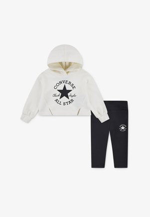 Witte cropped hoodie met zwart bedrukte sterlogo en tekst, gecombineerd met zwarte leggings met een klein logo. Van katoenmix.
