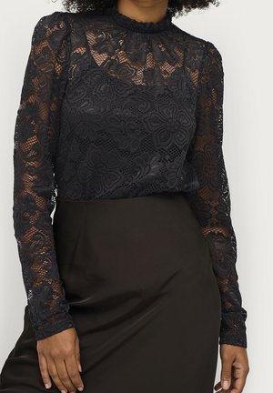 Sort blonder med lange ærmer og blomsterpatroner, båret stoppet ned i en højtaljet sort nederdel, der viser mellemtorso og arme.