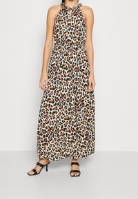 Robe longue à imprimé léopard en tissu léger, dotée d'un col halter, d'une taille froncée et d'une silhouette fluide. Portée avec des talons noirs à brides.