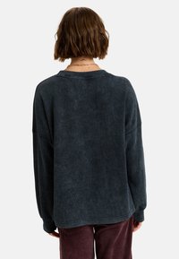 Donkergrijze, gestructureerde oversized trui met een bootnek en verlaagde schouders, gecombineerd met bordeauxrode corduroy broek. Zachte, casual stof.