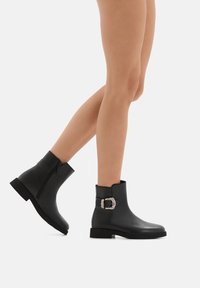 Stivaletti neri realizzati in pelle liscia, con zip laterale e un accento decorativo in metallo argentato sulla caviglia. Tacco basso a blocco.