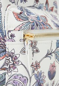 Biała syntetyczna torba w kwiatowy wzór, wyposażona w złoty zamek błyskawiczny, o teksturowanej powierzchni i żywych niebieskich, różowych oraz fioletowych motywach kwiatowych.