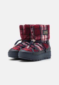 Czerwono-granatowe buty w kratę z futrzanym wierzchem, granatową gumową podeszwą i czarnymi sznurówkami. Posiadają złoty akcent z logo po boku.