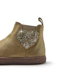 Botín de tobillo de ante dorado que presenta un gran acento de corazón brillante hecho de lentejuelas, con una suela de goma marrón texturizada y una pestaña de agarre.