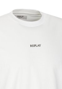 T-shirt bianca con un piccolo logo nero "REPLAY" vicino al collo, che mostra un design semplice e casual.