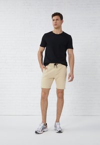 Sort kortærmet t-shirt parret med lyse beige shorts, der har elastisk talje med snoretræk. Båret med grå sportssko.