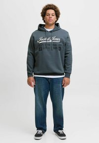 Grey cotton hoodie with logo and text on the front, paired with blue straight-leg jeans and black shoes with white laces.