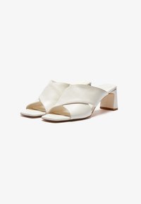 Hvite lærheler med en kryssbånddesign, �åpen tå og firkantet hæl. Glatt tekstur og minimalistisk stil.