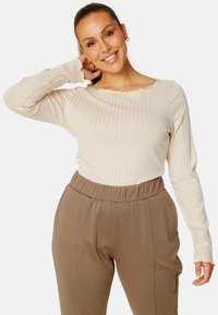 Lichtbeige geribbelde top met lange mouwen en een gegolfde halslijn, gecombineerd met hoge, bruine broek met een elastische tailleband.