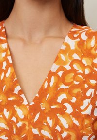 Un vestido de estampado naranja y blanco que presenta un escote en V y un diseño fluido, confeccionado con una tela ligera de textura suave.