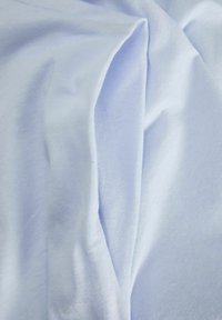 Tela de algodón azul claro que muestra una textura suave, con pliegues caídos que crean curvas suaves. Apariencia lisa sin patrones ni acentos.