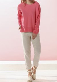 Rosa gestrickter Pullover mit langen Ärmeln, lässige Passform; kombiniert mit hellbeigen Leinenhosen und neutralen Espadrilles.