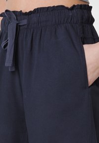 Marinblå, lätta joggers med elastisk midja, rynkdetaljer, justerbar dragsko och sidofickor. Slät textur.