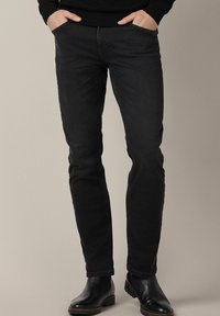 Czarne dżinsy o dopasowanym kroju, z klasycznym pięciopocketowym fasonem i subtelną teksturą. Noszone z czarnymi botkami za kostkę.