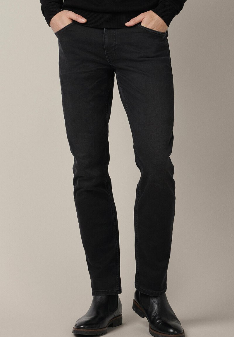Czarne dżinsy o dopasowanym kroju, z klasycznym pięciopocketowym fasonem i subtelną teksturą. Noszone z czarnymi botkami za kostkę.