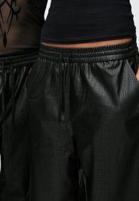 Μαύροι παντελόνες από συνθετικό δέρμα με υφή που μοιάζει με δέρμα κροκόδειλου, με ελαστική μέση και πλαϊνές τσέπες.