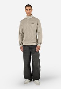 Beżowy sweter typu golf z długimi rękawami, z lekkim rozciągliwym materiałem. W połączeniu z luźnymi ciemnoniebieskimi dżinsami i białymi trampkami.
