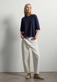 Marineblauw katoenen T-shirt met brede korte mouwen, gecombineerd met witte losse broek. Beigekleurige veterschoenen maken de outfit compleet. Eenvoudige, casual uitstraling.