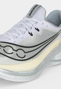 Άσπρο και γκρι παπούτσι για τρέξιμο Saucony με μαύρο λογότυπο, επάνω μέρος από δίχτυ, λευκά κορδόνια και επενδεδυμένη μπεζ μεσόσολα, λοξή πλευρική όψη.