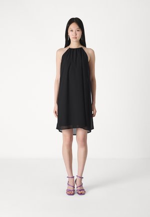 Abito nero con collo halter e silhouette fluida. Tessuto trasparente all'orlo. Indossato con tacchi a strappi viola. Design minimalista, senza motivi.