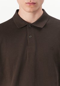 Bruine polo shirt van textuur stof, met een klassieke kraag, een drieknoopsgat en een klein geborduurd logo op de borst.