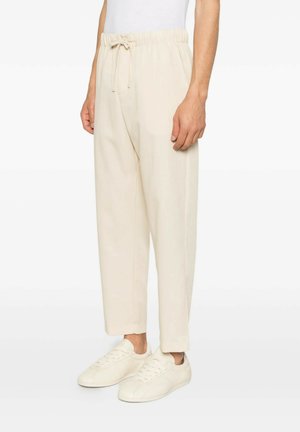Pantaloni beige casual con vita elastica e coulisse indossati con sneakers beige abbinate su una persona in piedi.