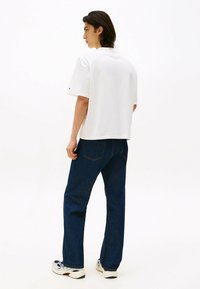 Hvid bomulds t-shirt med afslappet pasform, parret med mørkeblå denim jeans; outfittet er afsluttet med hvide og marineblå sneakers.
