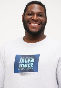 Grauer Hoodie mit einem blauen Grafikdesign und dem Text "JACK & JONES". Das Design umfasst diagonale Streifen und eine strukturierte Oberfläche.