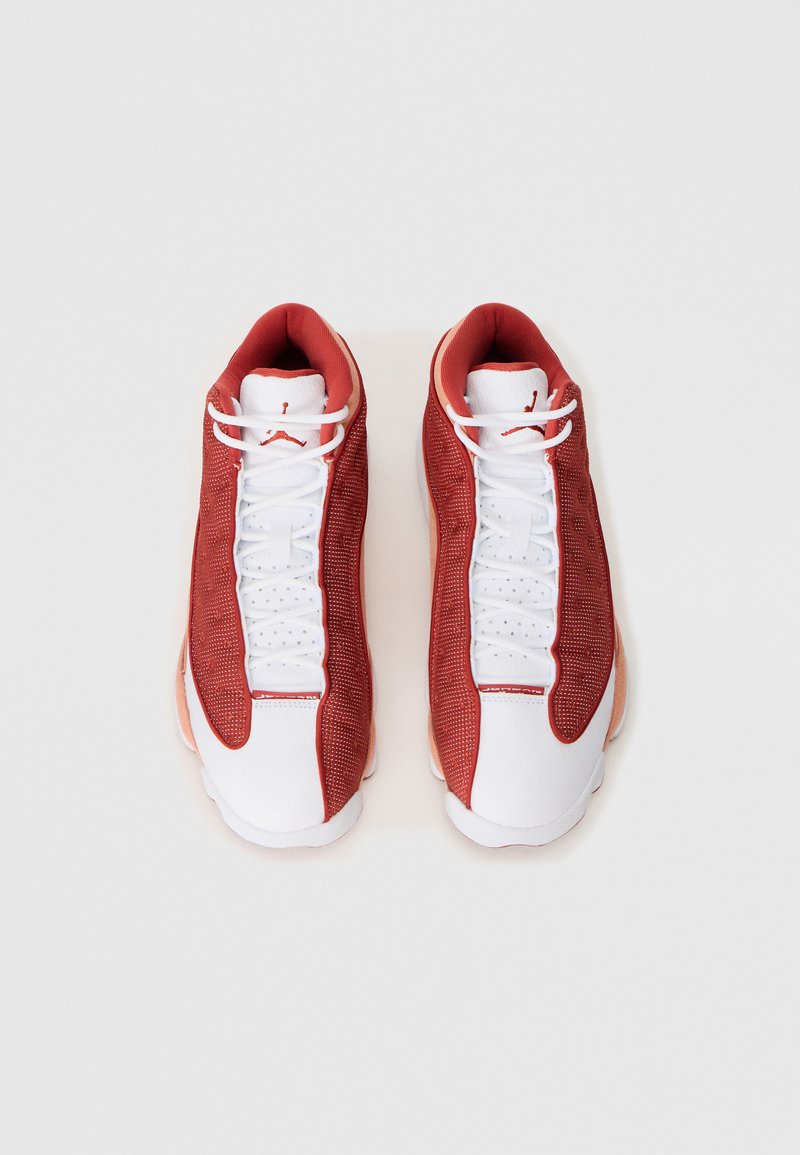 Scarpe da ginnastica rosse e bianche con tomaia in rete, accenti in pelle liscia, lacci piatti e motivo circolare sulla suola.