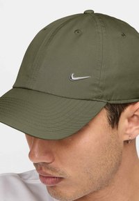 Sima anyagból készült olíva zöld sapka kerekített napellenzővel, hat panellel és egy kis fém Nike logóval az elején.