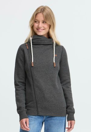 Sivá flísová mikina s vysokým golierom, drevenými akcentmi a nastaviteľnými šnúrkami. Má diagonálny zips a rebrované manžety.