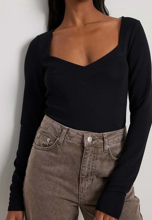 Long-sleeve black bodysuit with a v-shaped neckline, paired with high-waisted light brown corduroy pants featuring front pockets.