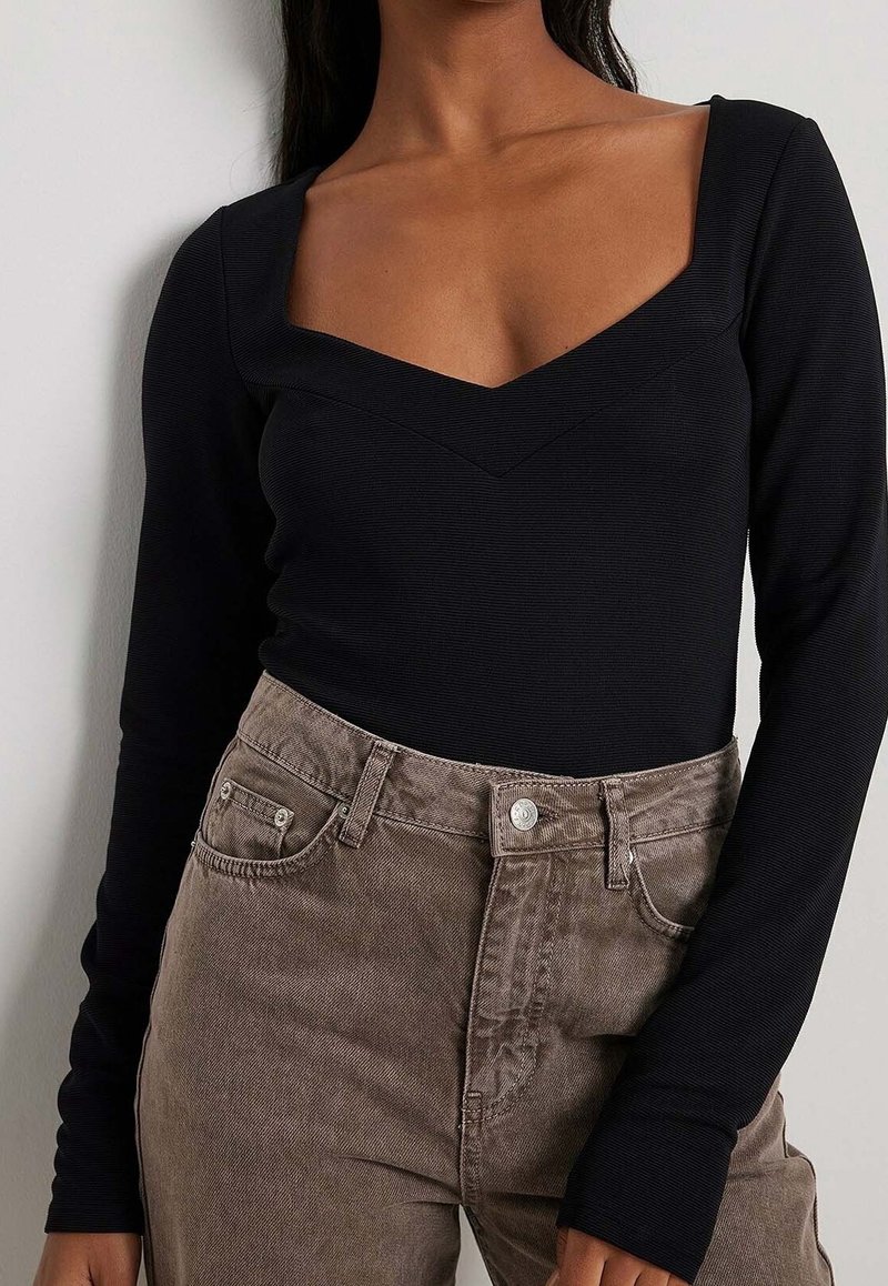Body a maniche lunghe nero con scollatura a V, abbinato a pantaloni in velluto a coste color marrone chiaro a vita alta con tasche frontali.