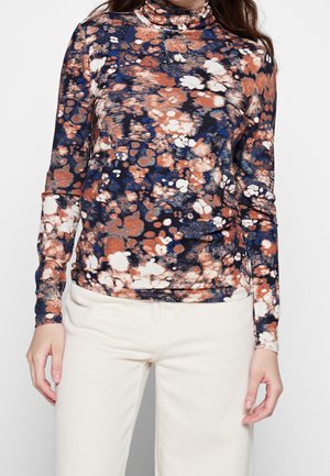Long-sleeve turtleneck top in navy, orange, and white abstract print. Soft, textured fabric with a fitted design. Paired with cream-colored pants.