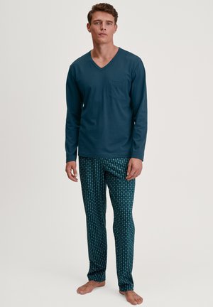 Marineblaue Langarm-V-Ausschnitt-Bluse mit Tasche, kombiniert mit gemusterten, schmal geschnittenen Hosen in dunklem Grün mit hellen Blumenmustern.