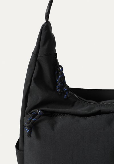 Sacul din țesătură neagră cu o textură netedă. Dispune de o buzunare cu fermoar și șnururi cu accente albastre. Design unghiular cu un vârf structurat.