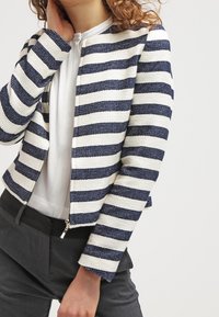 Pruhovaná bunda s tkanou strukturou, s námořnicky modrými a bílými vodorovnými pruhy, předním zipem a přiléhavým střihem.