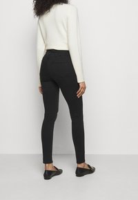 Jeans negros ajustados de cintura alta, con bolsillos traseros y una tela elástica. Combinados con un suéter crema y zapatos planos negros.