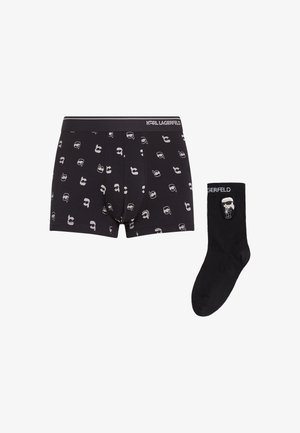 Black boxer shorts with gray face patterns and a logo waistband, paired with solid black socks featuring a graphic and logo.
