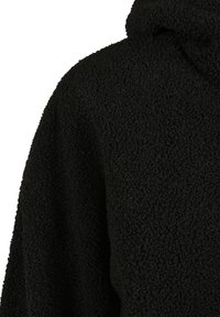 Gros plan d'un tissu polaire noir texturé sur l'épaule et le col d'un vêtement avec une surface douce et bouclée.