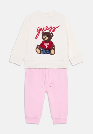 Krempullover med brodert bjørn og "guess"-tekst, paret med rosa bomulls-joggebukser med elastisk midje og mansjetter.