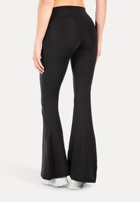 Zwarte flared leggings gemaakt van rekbaar materiaal, met een hoge tailleband en een gladde textuur, die afneemt naar een flared zoom bij de enkels.