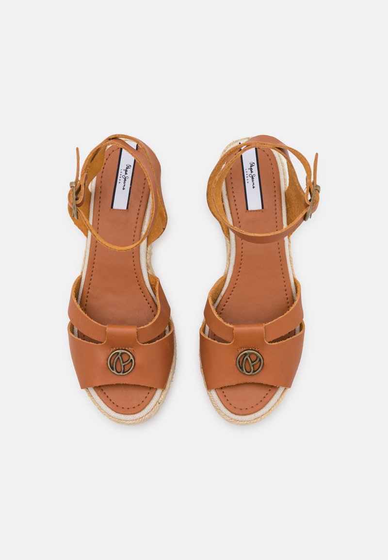 Sandalias de cuero marrón con tacón alto, punta abierta y tira en el tobillo. Presentan correas dobles a lo largo del pie y un acento metálico decorativo.