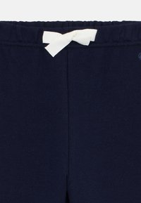 Námornícke modré nohavice s jemnou textúrou, majú elastický pás a biely stiahnuteľný šnúrka. Minimalistický dizajn, bez ďalších vzorov či akcentov.