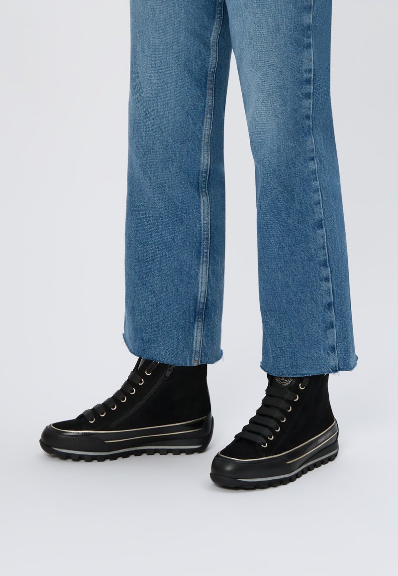 Czarne zamszowe wysokie botki z złotymi akcentami, z zamkiem błyskawicznym, gumową podeszwą i sznurowanym fasonem, połączone z niebieskimi dżinsami.