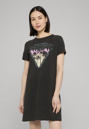 Vrouw met stijl zwart haar die een zwart jurkje met korte mouwen draagt, met een afbeelding van een palmbomen en de tekst "Pacific sunset" op de voorkant.