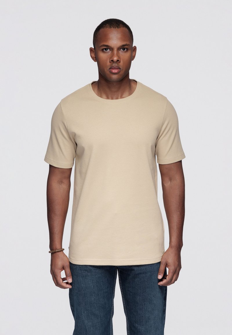 Béžové tričko s krátkým rukávem z bavlny, s kulatým výstřihem a texturovaným vzorem. Kombinováno s tmavými džínami.