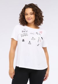 Femeie cu păr creț, purtând un tricou alb cu desene mici negre și roșii, inclusiv inimi, valuri, un umeraș și cuvântul "Salut!"